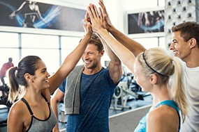 Smiling men and women doing high five in gym. Group of young people making high five gesture in gym after workout. Happy successful fitness class after training.