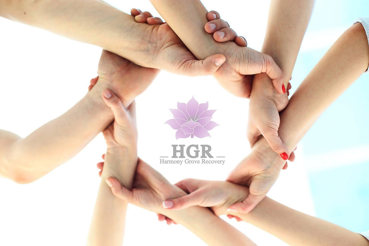View of people's hands in a circle with Harmony Grove Recovery logo in the center
